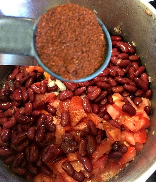 Photo of chili powder in a measuring spoon being added to a large pot of chili