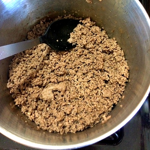 Photo of cooked ground beef in a large pot with a black spoon