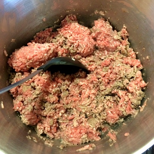 Photo of raw ground beef in a large pot with a black spoon