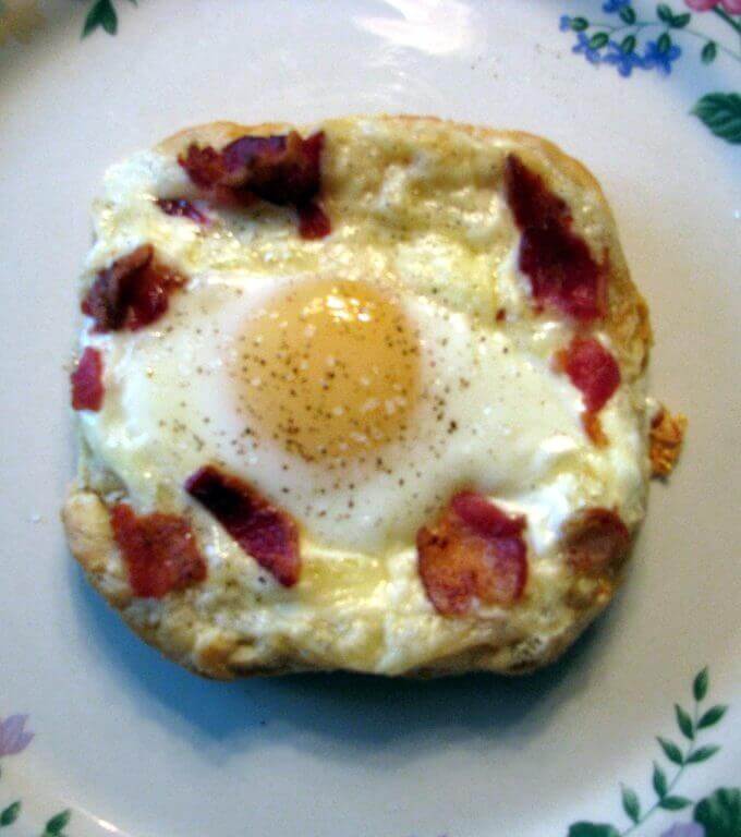 Plated Cheesy Egg and Bacon Puff Pastry Tart with a sunny side up egg crumbled bacon and shredded cheese on a baked puff pastry