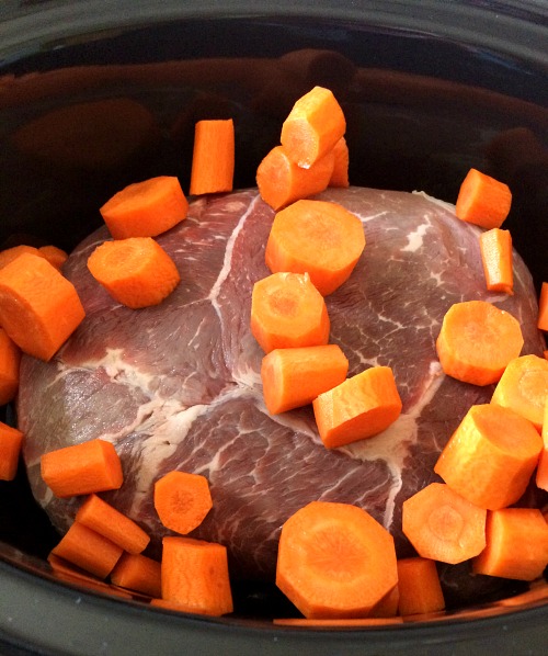 Photo of uncooked roast beef and sliced carrots in a black slow cooker