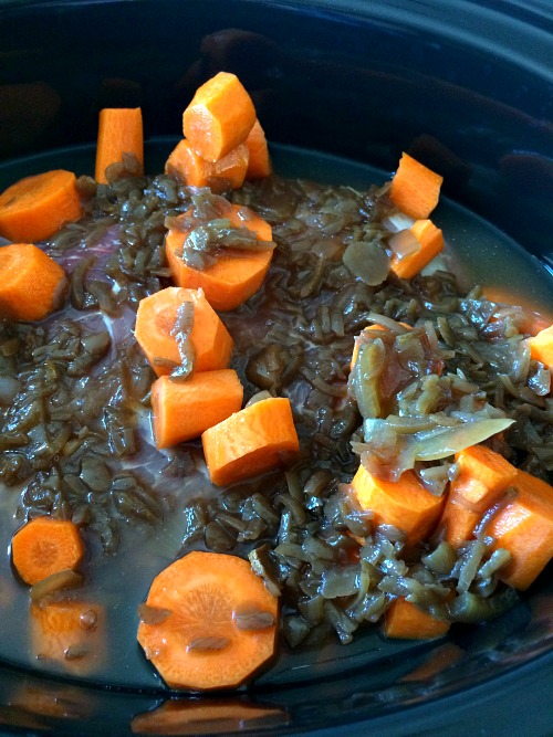 photo of uncooked roast beef with carrots and French onion soup in a black slow cooker