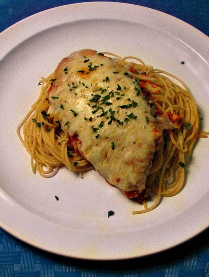 Photo of plated Chicken Parmesan over thin spaghetti on a white plate with a blue place mat