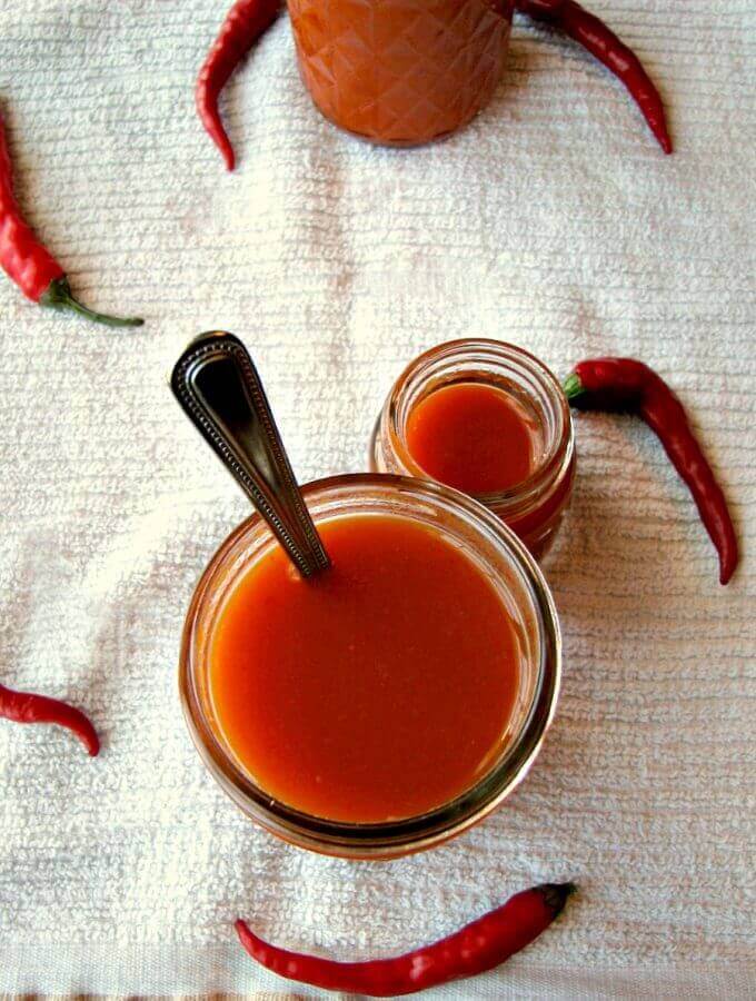 Photo of Homemade Cayenne Pepper Sauce in a mason jar on a white cloth with cayenne peppers scattered around the mason jar