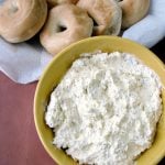 Photo of Easy Everything Bagel Dip a white creamy dip in a yellow bowl next to a basket of bagels on a brown table