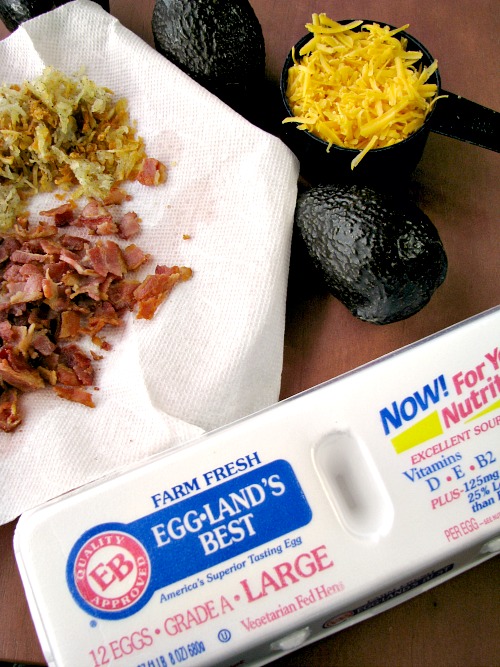 Photo of a display of a carton of Eggland's Best eggs next to a plate of crumbled bacon and fried hash brown potatoes, whole avocados and a cup of shredded cheese