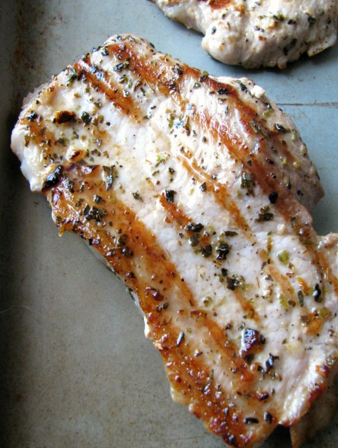 Close-up photo of one Garlic Herb Grilled Pork Chop on a silver baking pan