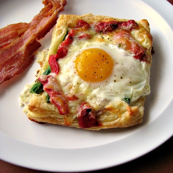 Photo of plated Roasted Red Pepper Asparagus Egg Tart on a white plate next to two slices of bacon