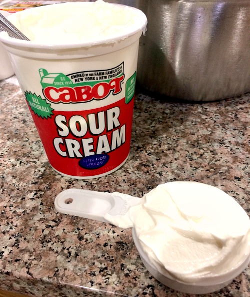 Photo of a measuring cup full of Cabot sour cream next to the container of sour cream