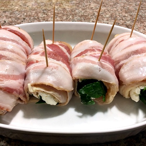 Photo of bacon wrapped stuffed chicken breasts in a white baking dish