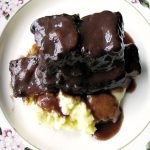 photo of plated Slow Cooker Red Wine Braised Short Ribs over mashed potatoes on a white flower trimmed plate