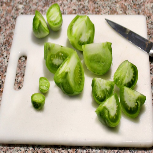 photo of sliced green tomatoes on a white cutting board with a knife on the right side