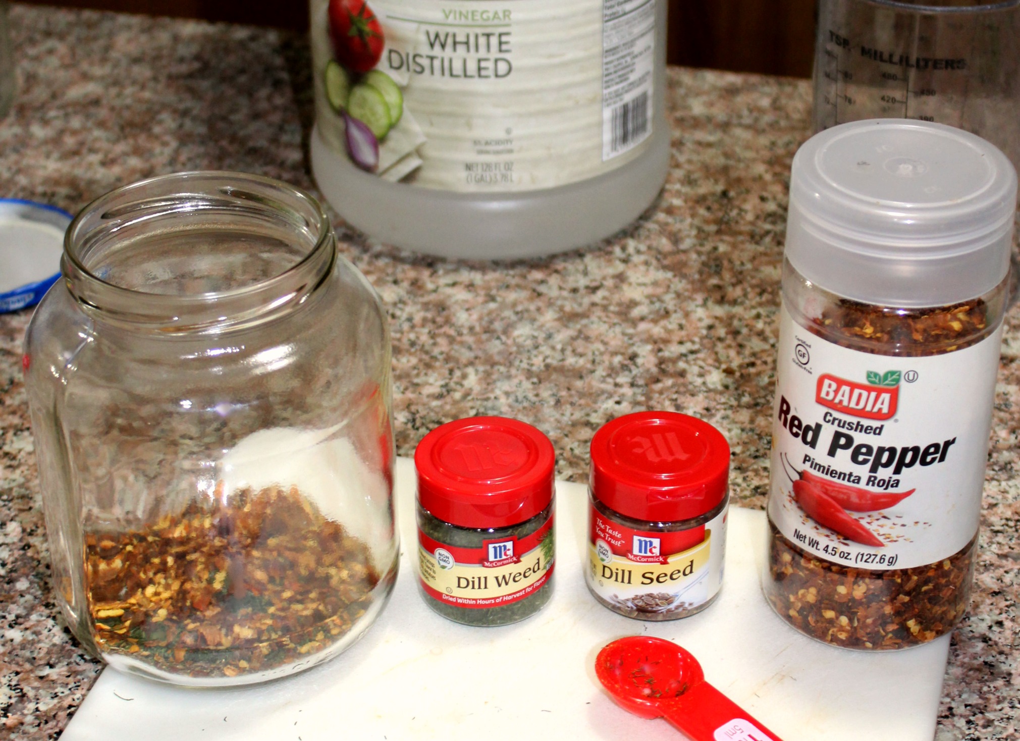 photo of pickling spice, red pepper flakes in a jar, and small bottles of dried dill weed and dill seed with a bottle of vinegar in the back