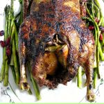 Overhead photo of a whole Crispy Roast Duck on a white platter with asparagus and cranberries