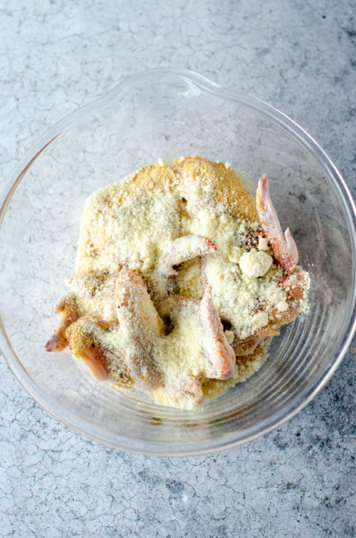parmesan cheese on top of chicken wings in a glass bowl